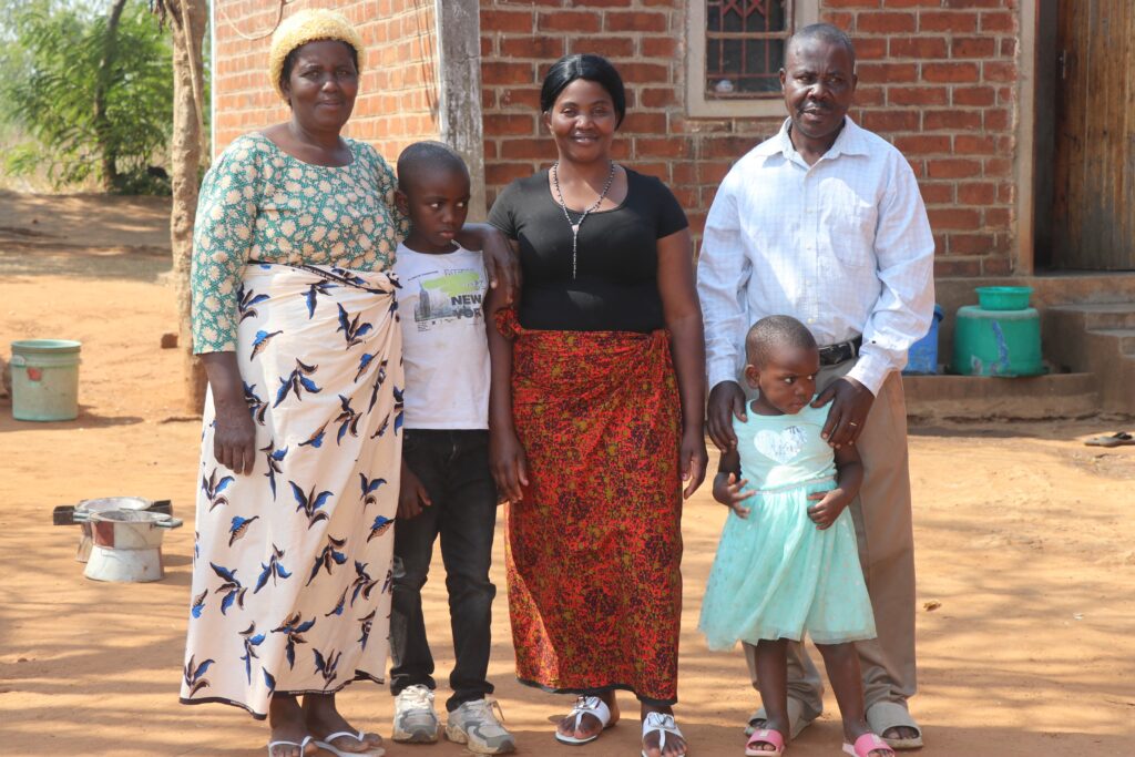 Maggie Chisoni stands with her parents and two children outside their family home in Malawi.