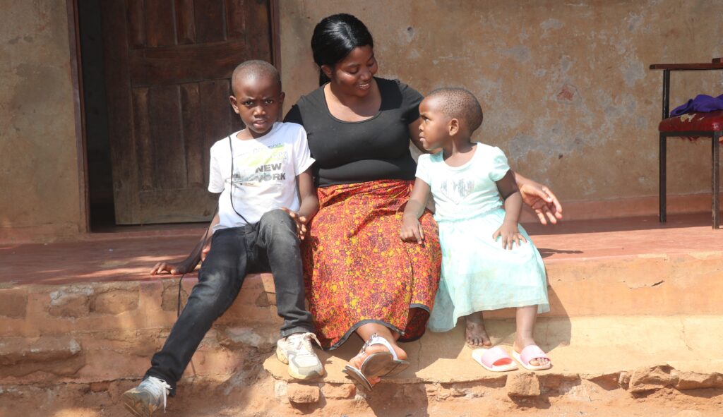 Maggie Chisoni sits with her young son and daughter outside their home in Malawi.
