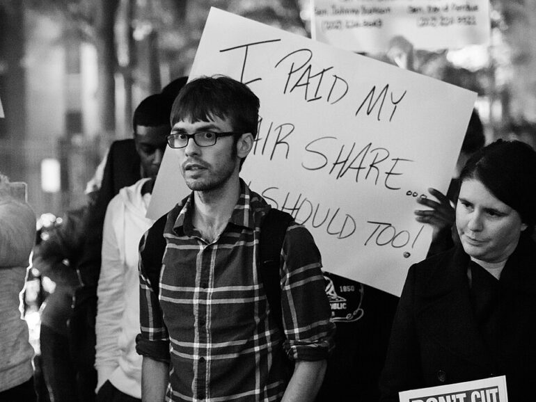 Sign reading "Tax Cuts for 1% = Budget Cuts for 99%" at a public demonstration.
