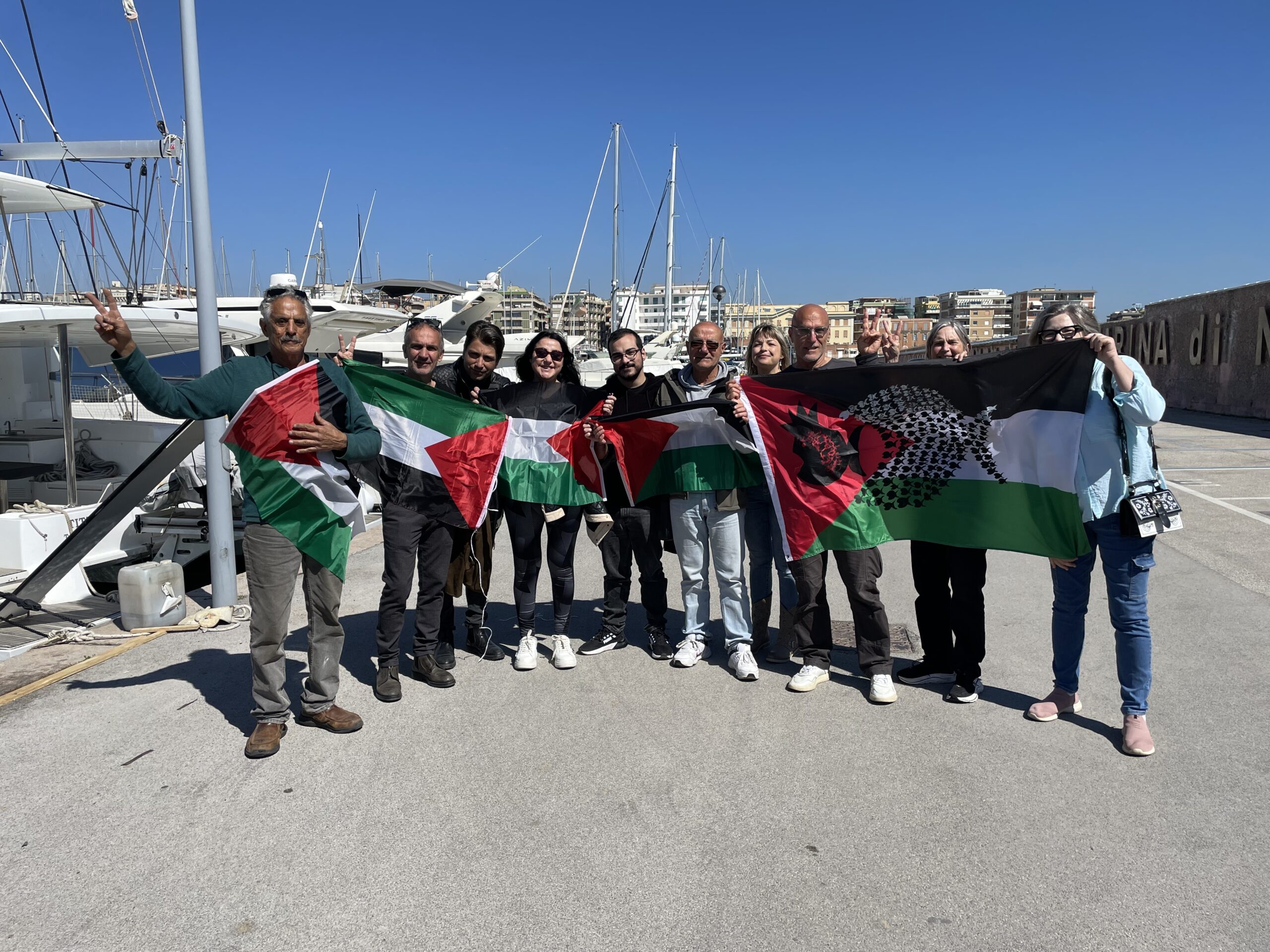 Flotilla participants holding Palestinian flags at a marina in Italy
