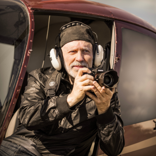 Donn Delson at the edge of a helicopter capturing the view