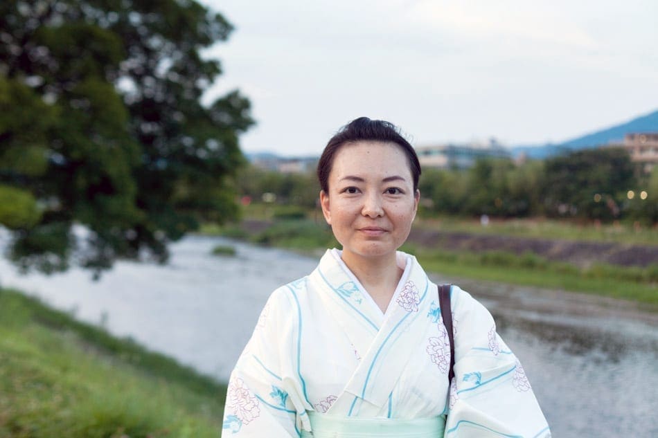 A woman poses in a kimono in front of a river.