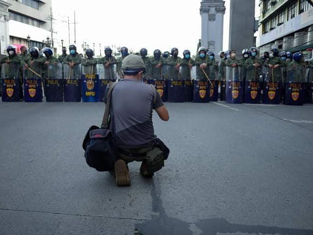 Photojournalist faces a barricade of police officers wearing protective gear and riot shields