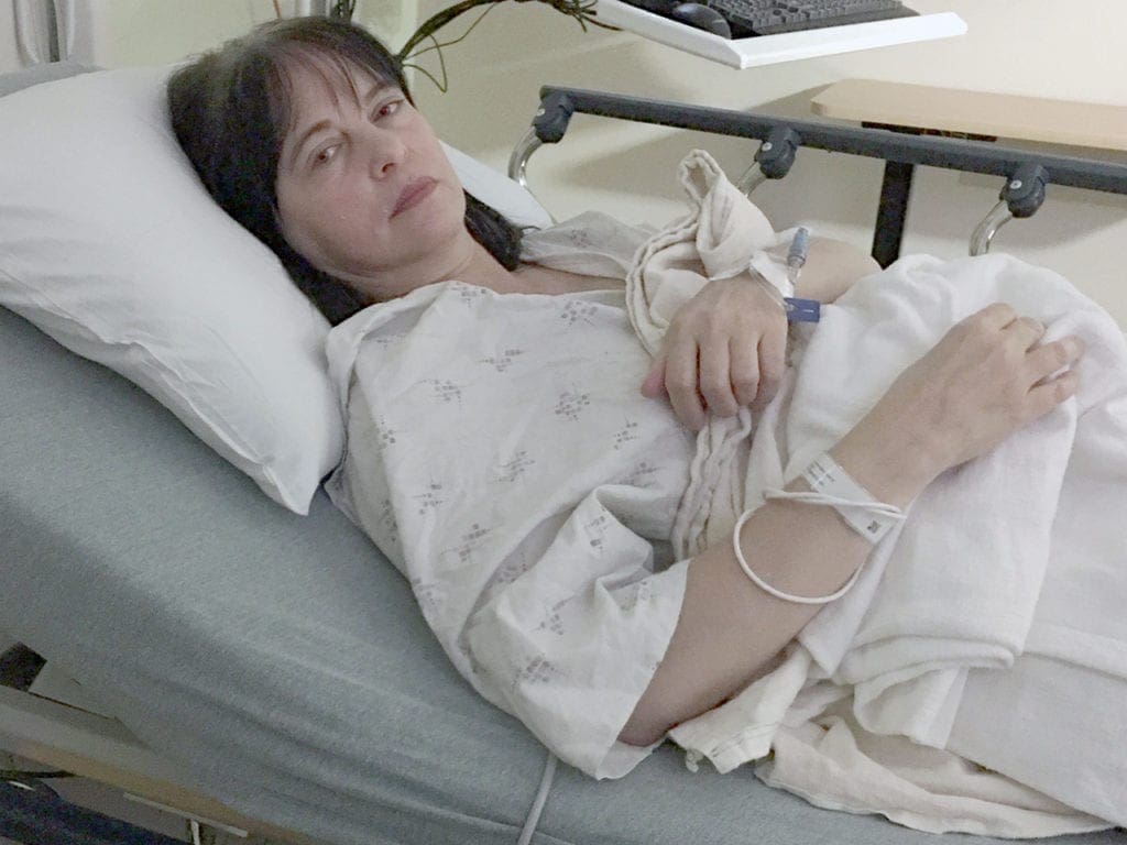 A woman dressed in a white hospital gown is in bed waiting for surgery.