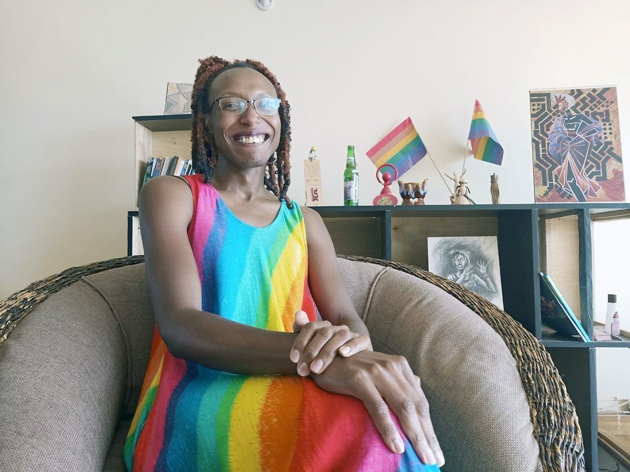 Arya Jeipea Karijo wears a rainbow dress in her living room while sitting with her arms crossed.