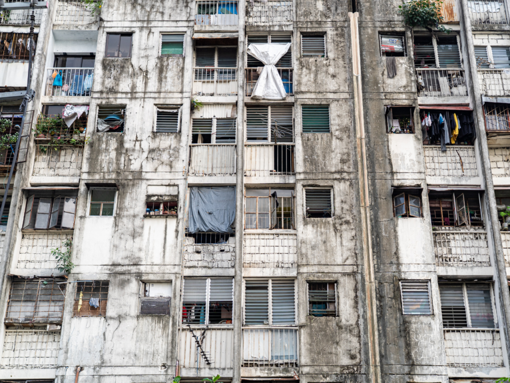 The tenement’s exterior shows its age and neglect – walls cracked, windows patched with tarps, and laundry hanging from every balcony. 